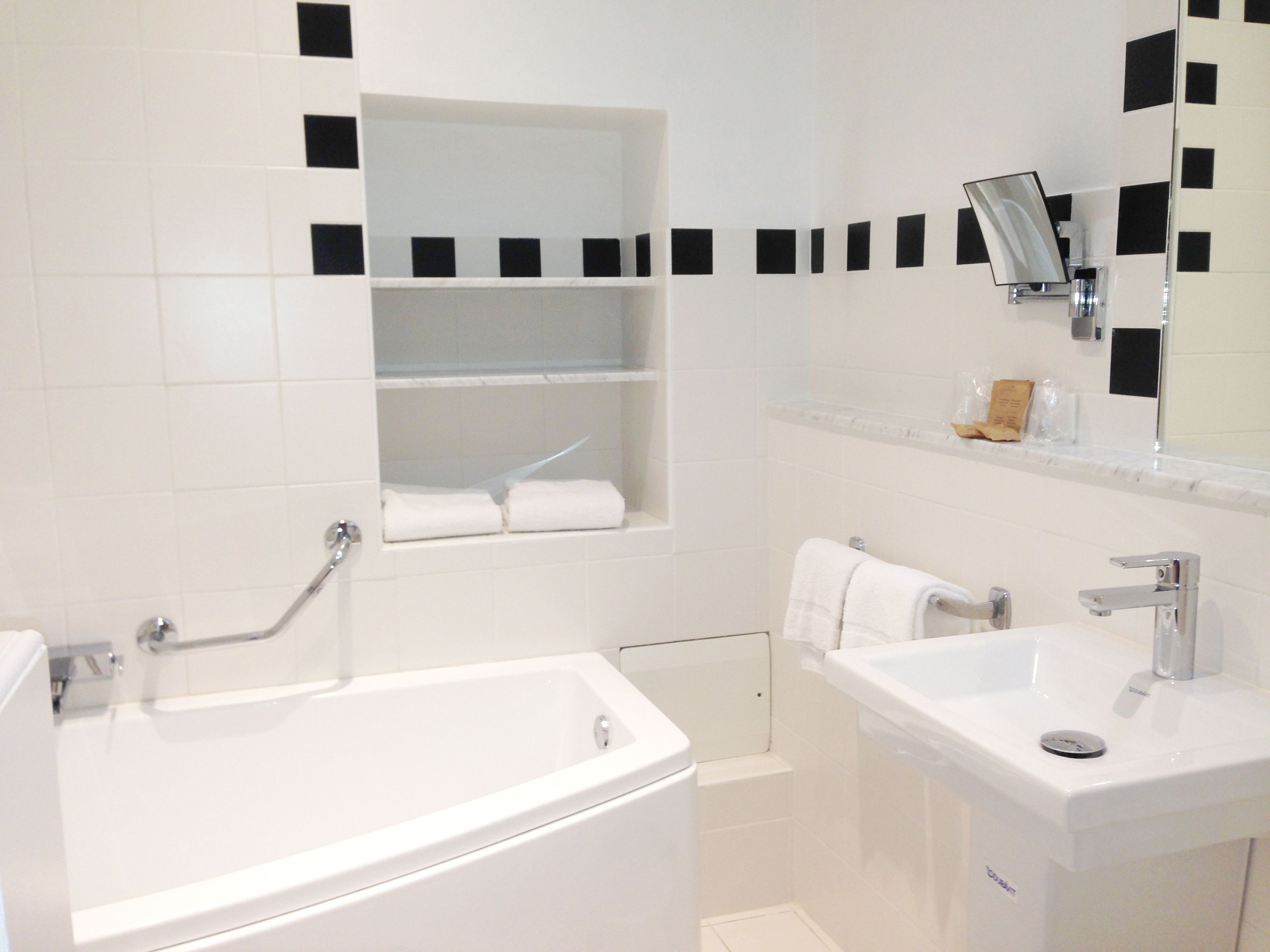 A bathroom with a bathtub, a sink, and a mirror. There are shelves above the bathtub and a towel rack next to the sink.