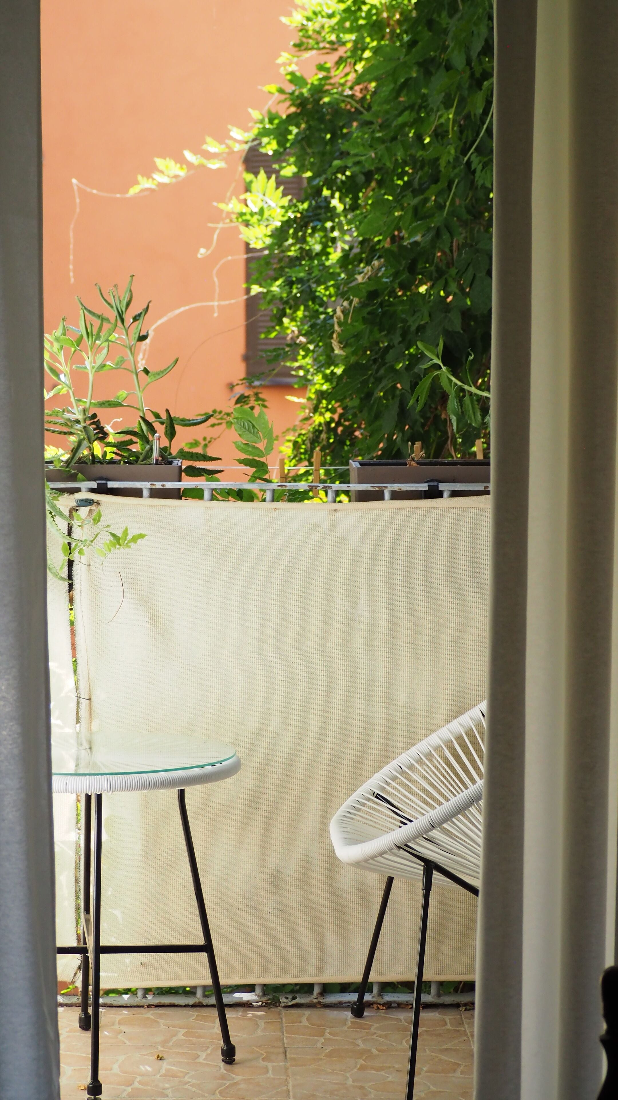 A patio area with a white metal table and chair, a beige woven privacy screen, and a stone floor.