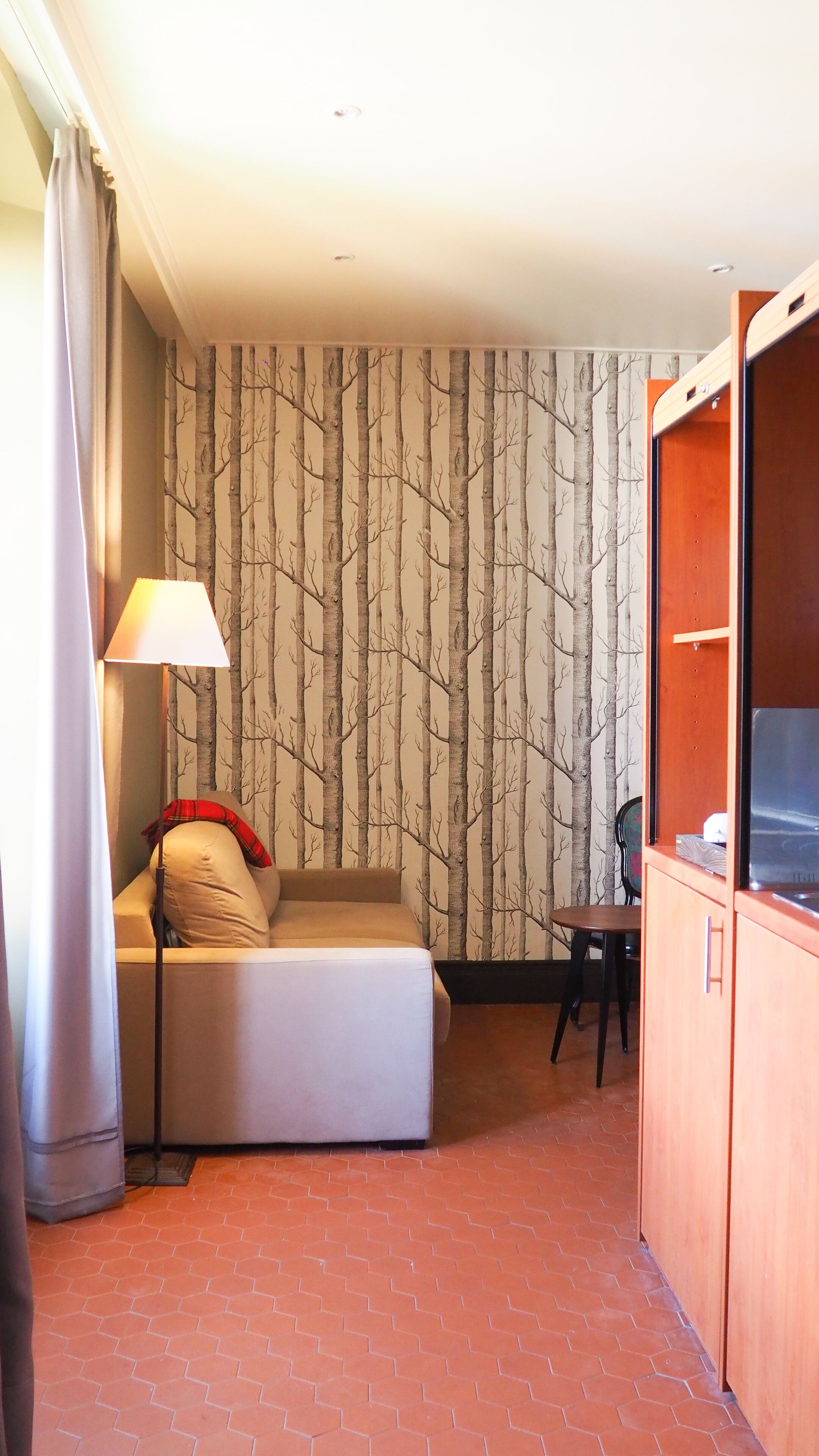A compact room with a sofa bed, a small table, a lamp, and a wardrobe.