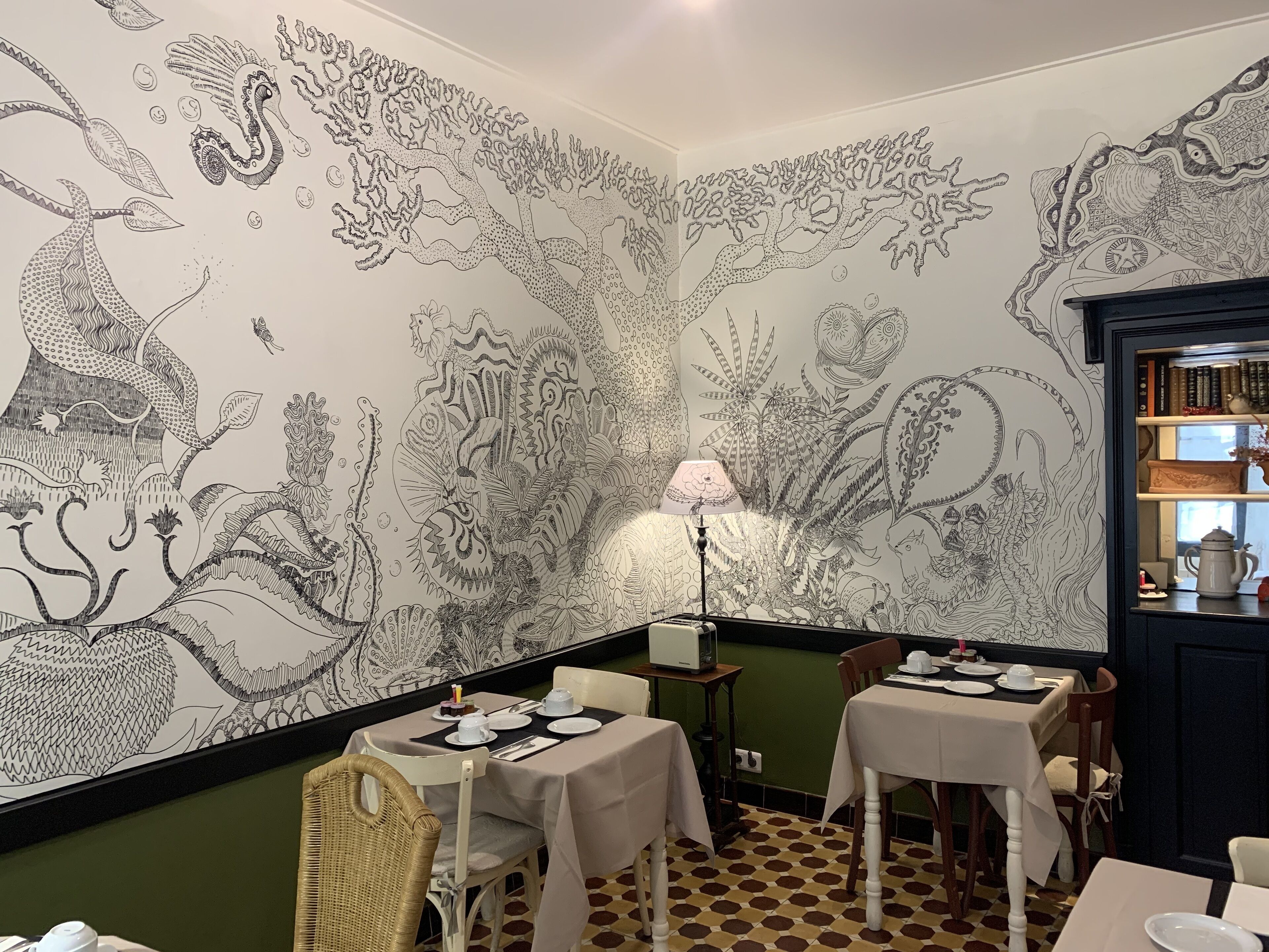 Un comedor con mesas dispuestas para una comida, una lámpara y una estantería con libros y objetos decorativos.