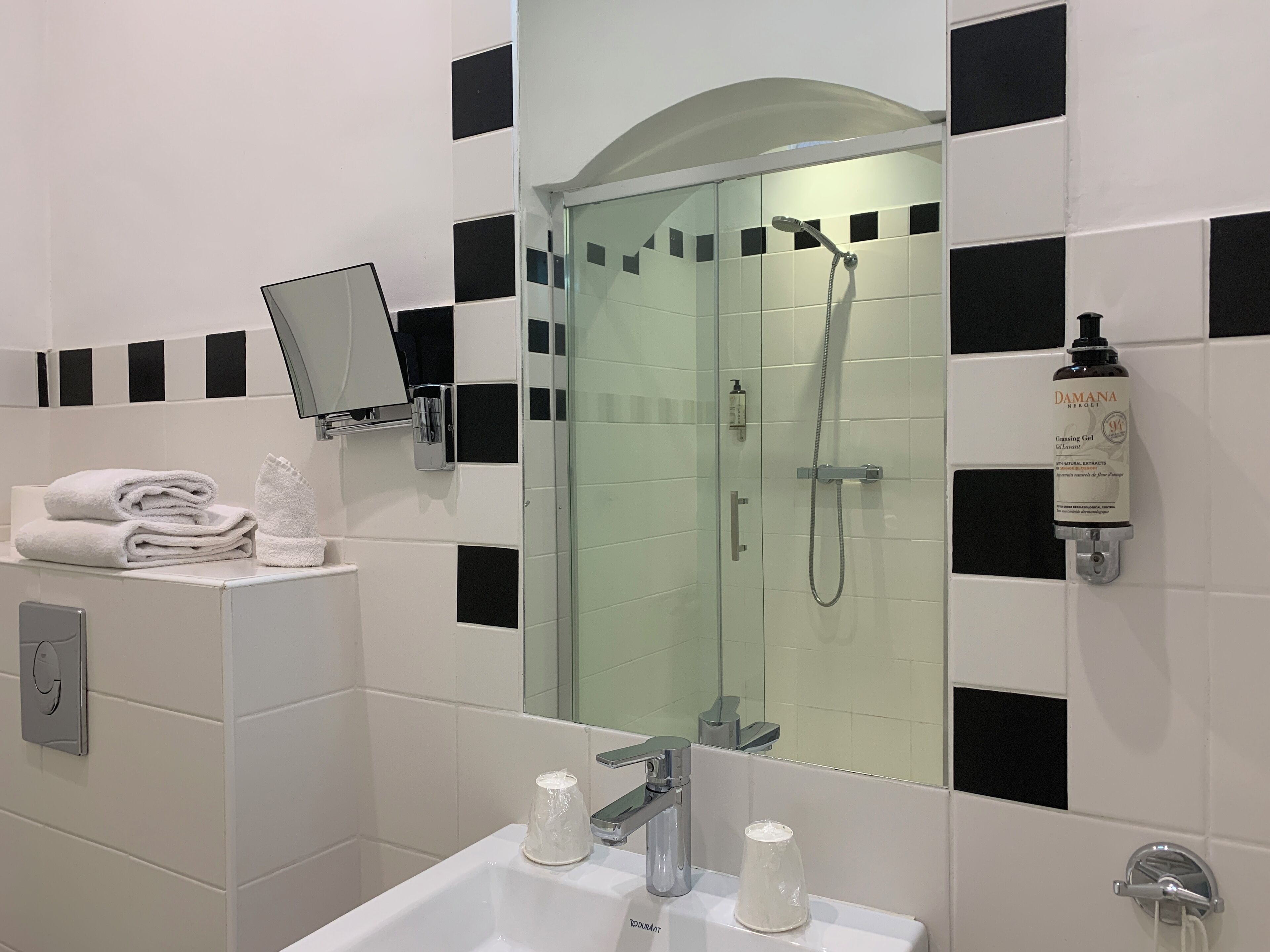 A modern bathroom with a glass-enclosed shower, a sink with two faucets, and a mirror mounted on the wall.
