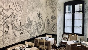 A dining area with a black and white patterned wall, tables with white tablecloths, and chairs. - Hotel Central Bastia (Bastia)