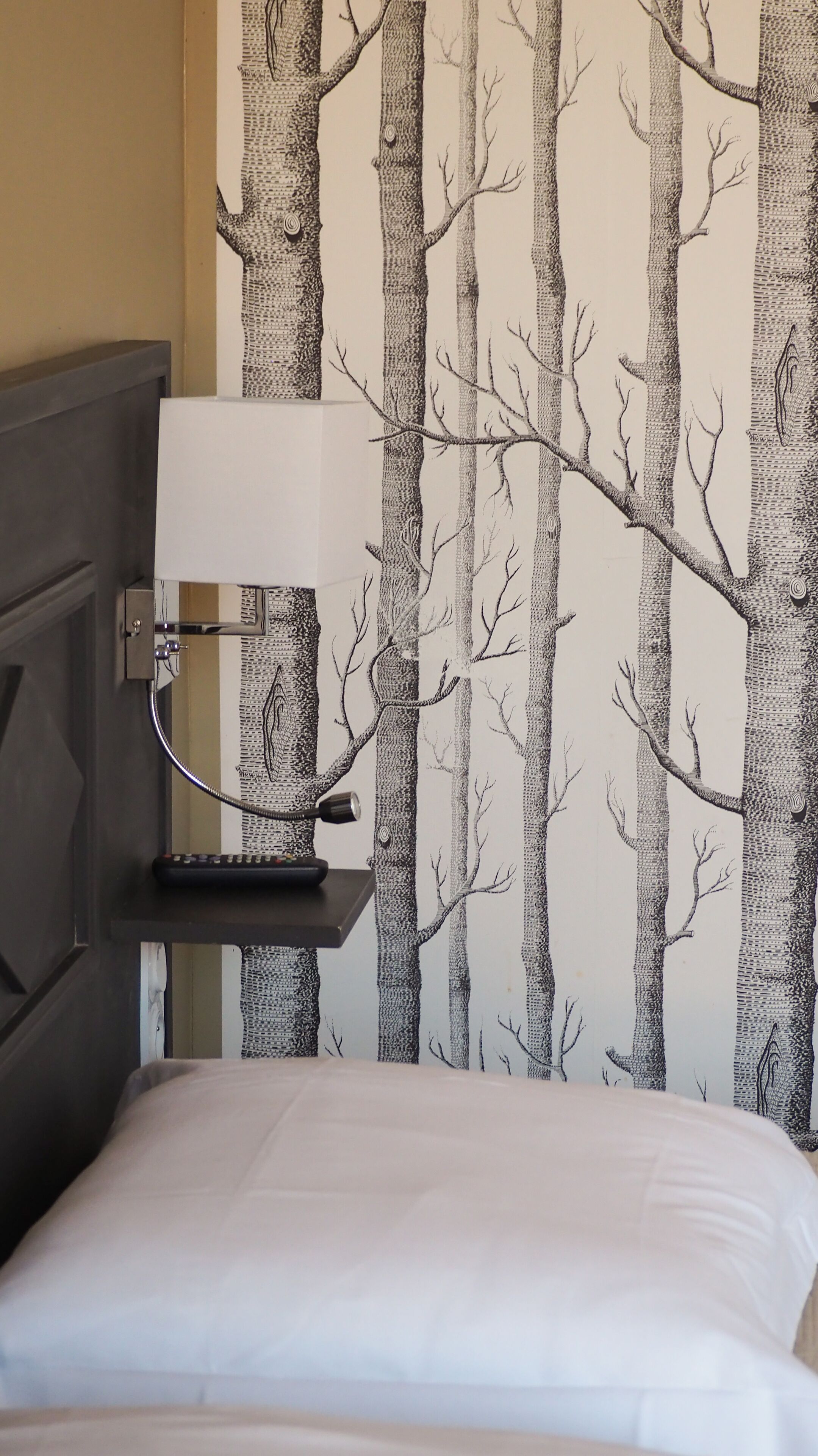 Un dormitorio con una cama, una mesita de noche con lámpara y una pared con diseño de árbol.