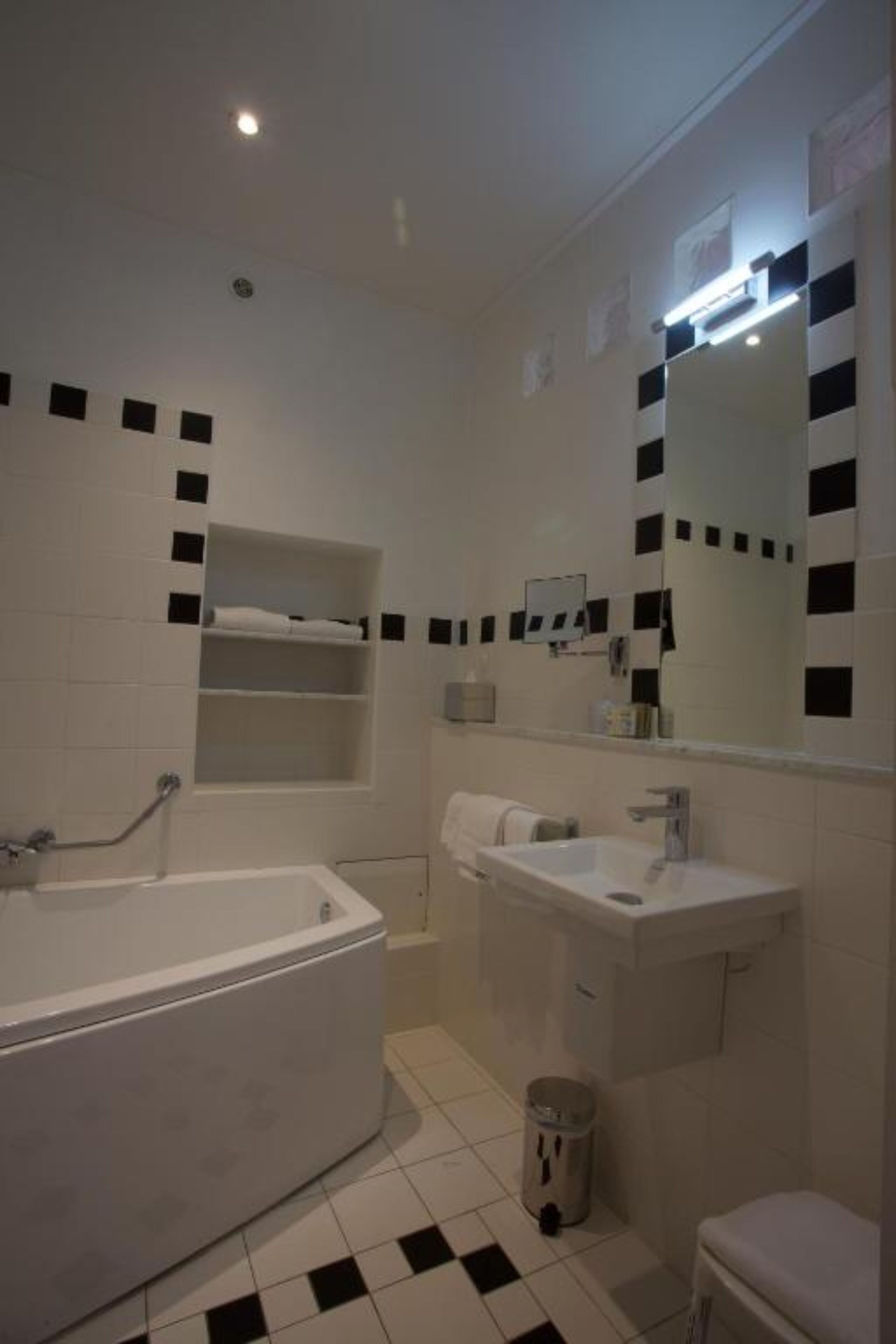Une salle de bain avec une baignoire, un lavabo et des toilettes. Il y a des étagères au-dessus de la baignoire et une poubelle près des toilettes.