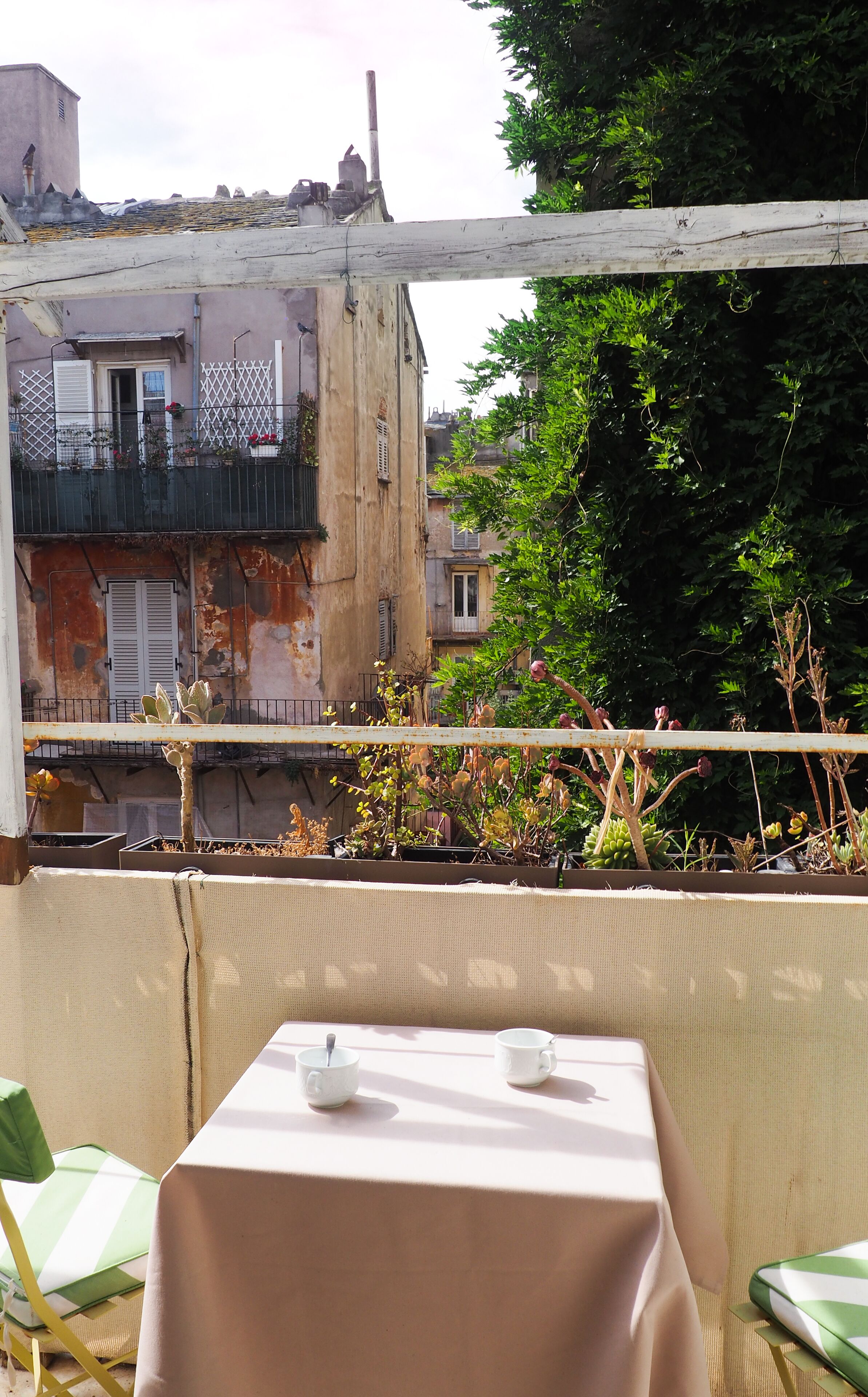 A terrace with a table set for two, overlooking a cityscape with buildings and greenery.