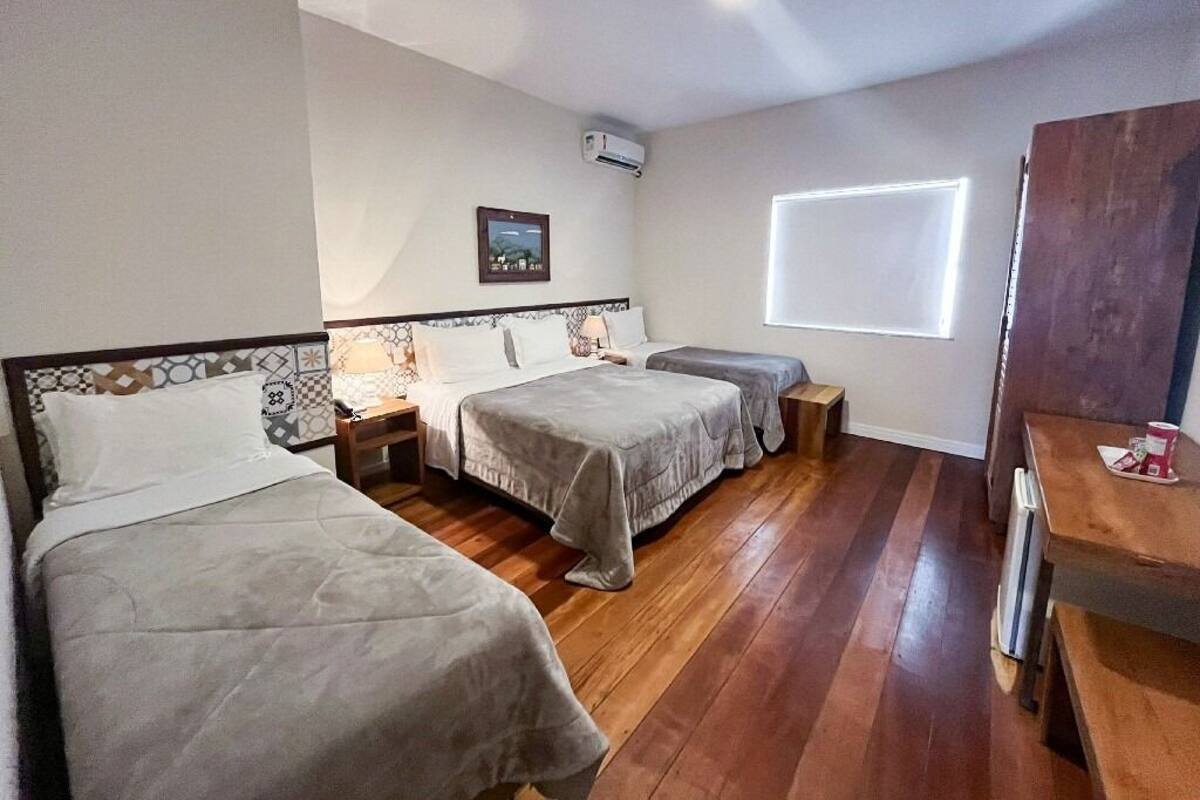 Una habitación de hotel con dos camas individuales, piso de madera, una mesita y una ventana.