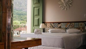 Une chambre à coucher avec un lit, une table de chevet, une lampe et une vue sur un paysage montagneux, visible à travers une porte ouverte.