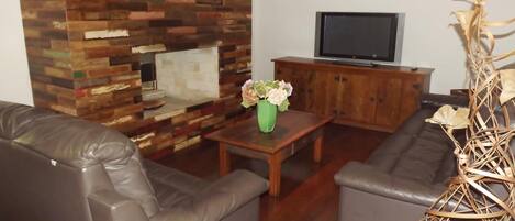 A living room with a wooden wall, a television, a sofa, and a coffee table with flowers.