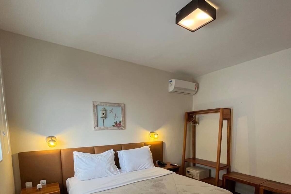 Un dormitorio con cama, mesitas de noche, aire acondicionado instalado en la pared y un espejo.