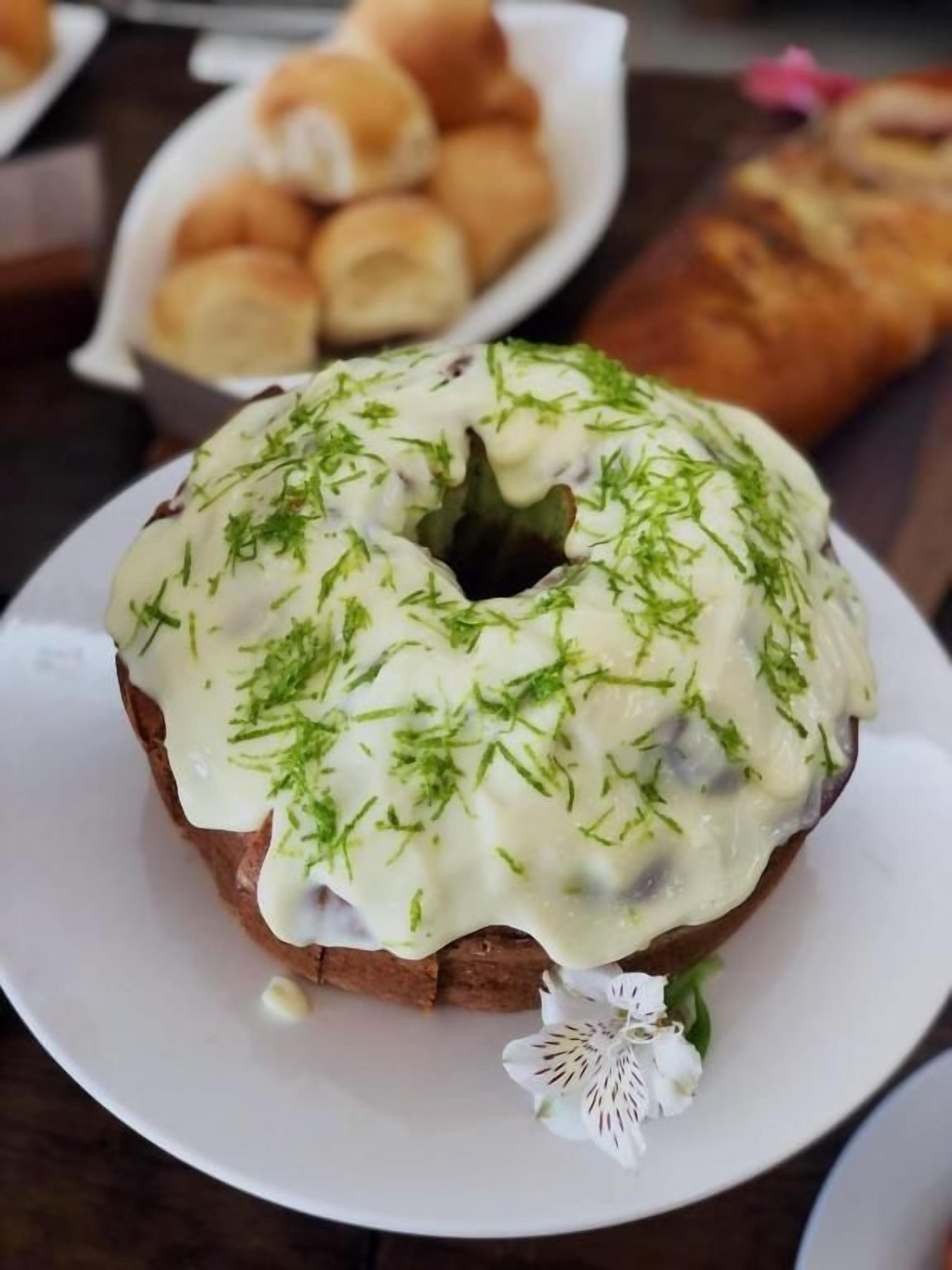 A food item on a plate with a garnish, and a basket of rolls in the background.