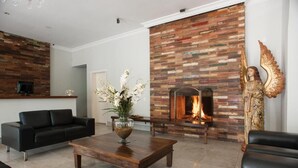 Un salon moderne avec une cheminée, des canapés en cuir noir, une table basse en bois et une statue d’ange décorative.