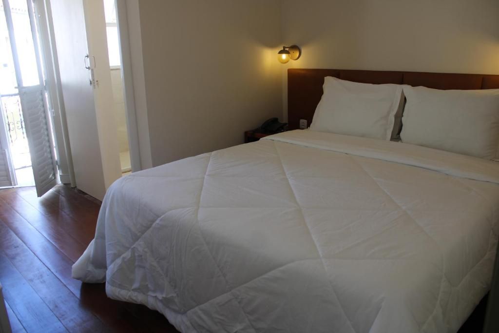 A hotel room with a large bed, a nightstand, a wall-mounted light, and a door leading to an outdoor area.