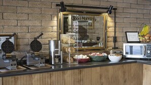 Una barra de desayuno con máquinas para hacer gofres, una cafetera y un microondas.