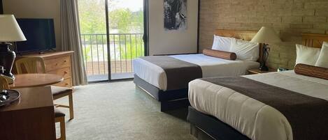 Une chambre d’hôtel avec deux lits, un bureau, une chaise, une télévision et un balcon donnant sur un espace verdoyant.