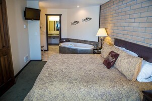 Habitación de hotel con una cama grande, una zona de estar, un baño con bañera y un televisor montado en la pared.