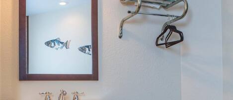 Un baño con un lavamanos blanco, un espejo con una obra de arte de peces, un perchero con toallas dobladas y un tendedero de metal.