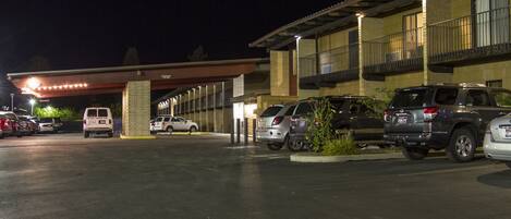 Un estacionamiento con varios automóviles y un edificio con acceso cubierto.