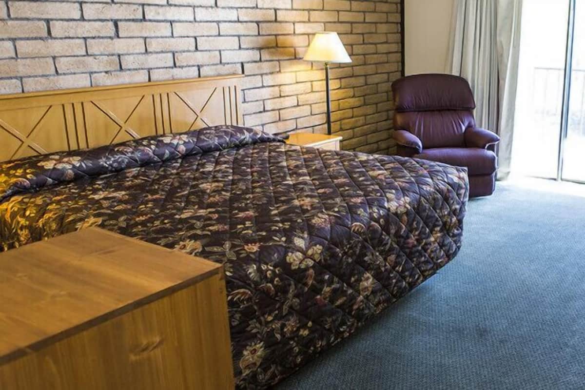 A hotel room with a large bed, a chair, a desk, and a window with a view.