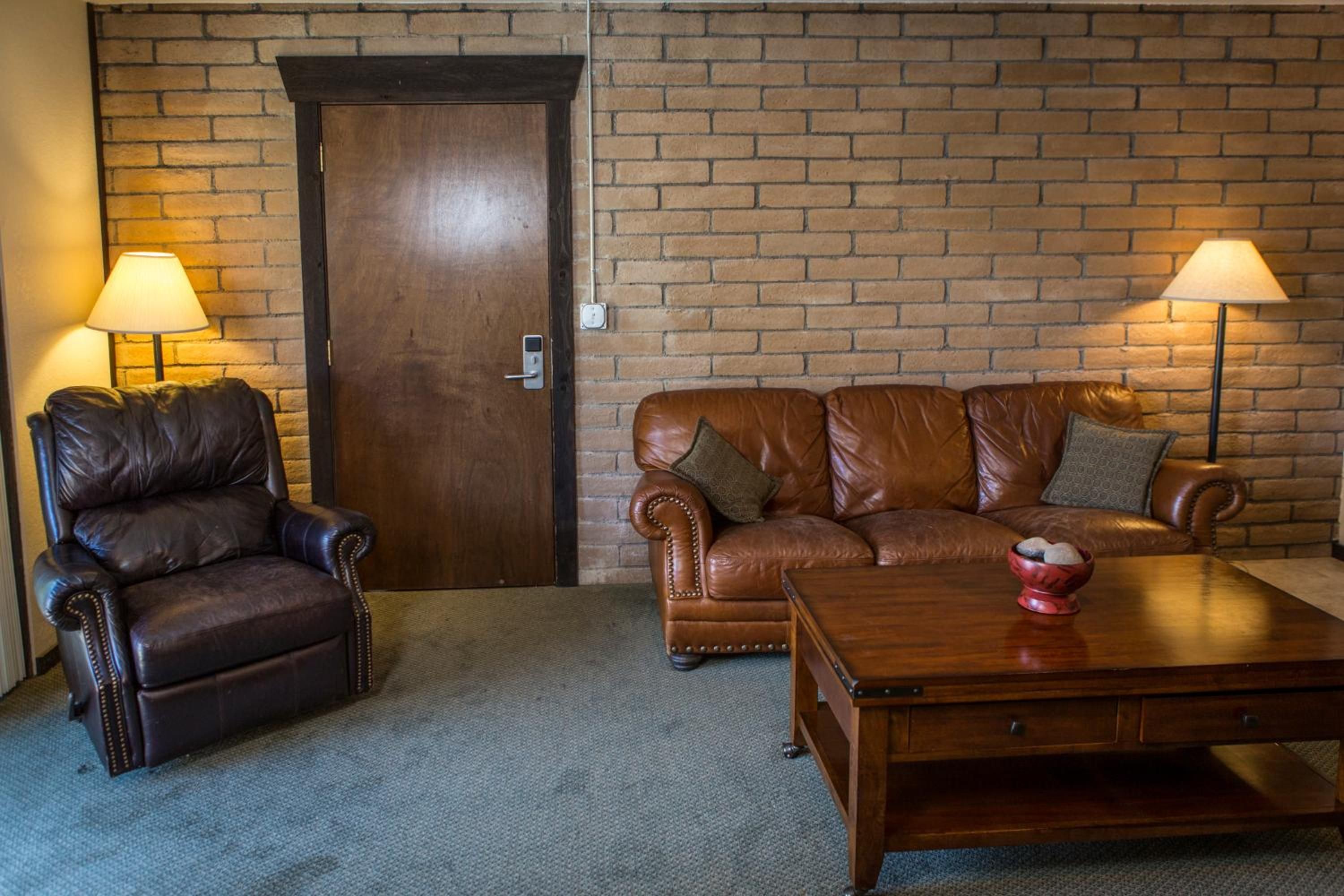 A room with a leather armchair, a sofa, a wooden coffee table, and two floor lamps.