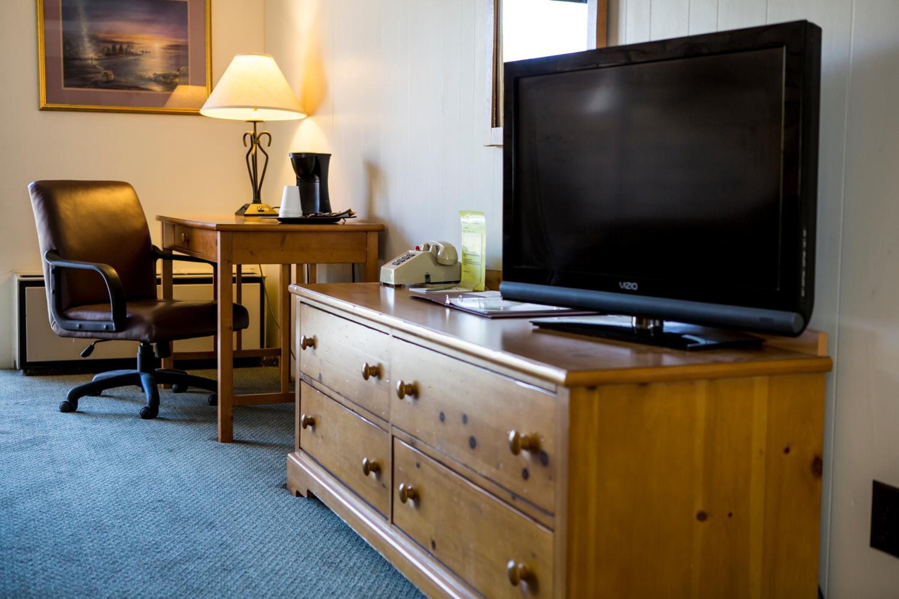 Una habitación de hotel con un aparador de madera, televisor, escritorio con lámpara y una silla.