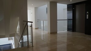 Un interior moderno con barandilla de cristal, suelo pulido y puerta de ascensor oscura.