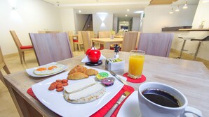 Desayuno con cruasanes, huevos, salchichas y una taza de café sobre una mesa.