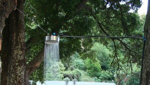 A person in a white bikini standing in a circular brick water feature with a shower head above. - River Valley Lodge (Pukeokahu)