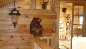 Un interno in legno con una scultura di orso su una ringhiera, una testa di cervo appesa al muro e un arredamento rustico.
