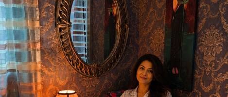A room with a large ornate mirror, a small table with a lamp, and a painting on the wall.