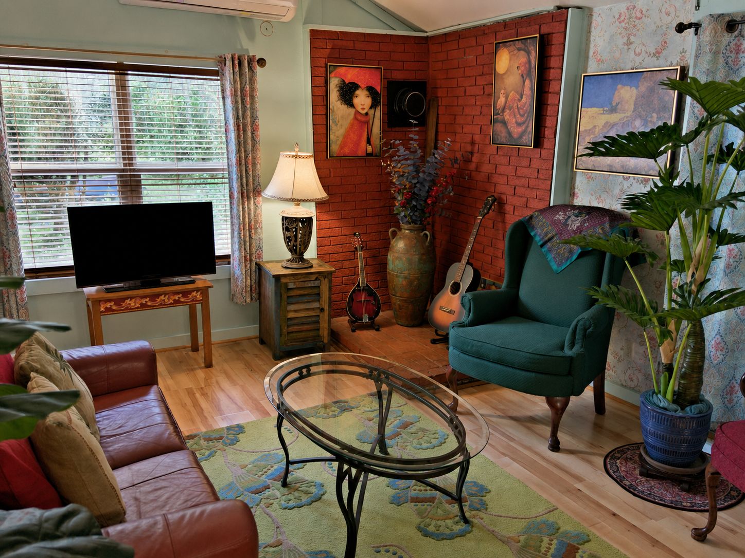 A living room with a television, a green armchair, a glass coffee table, a red brick wall, and a large plant.