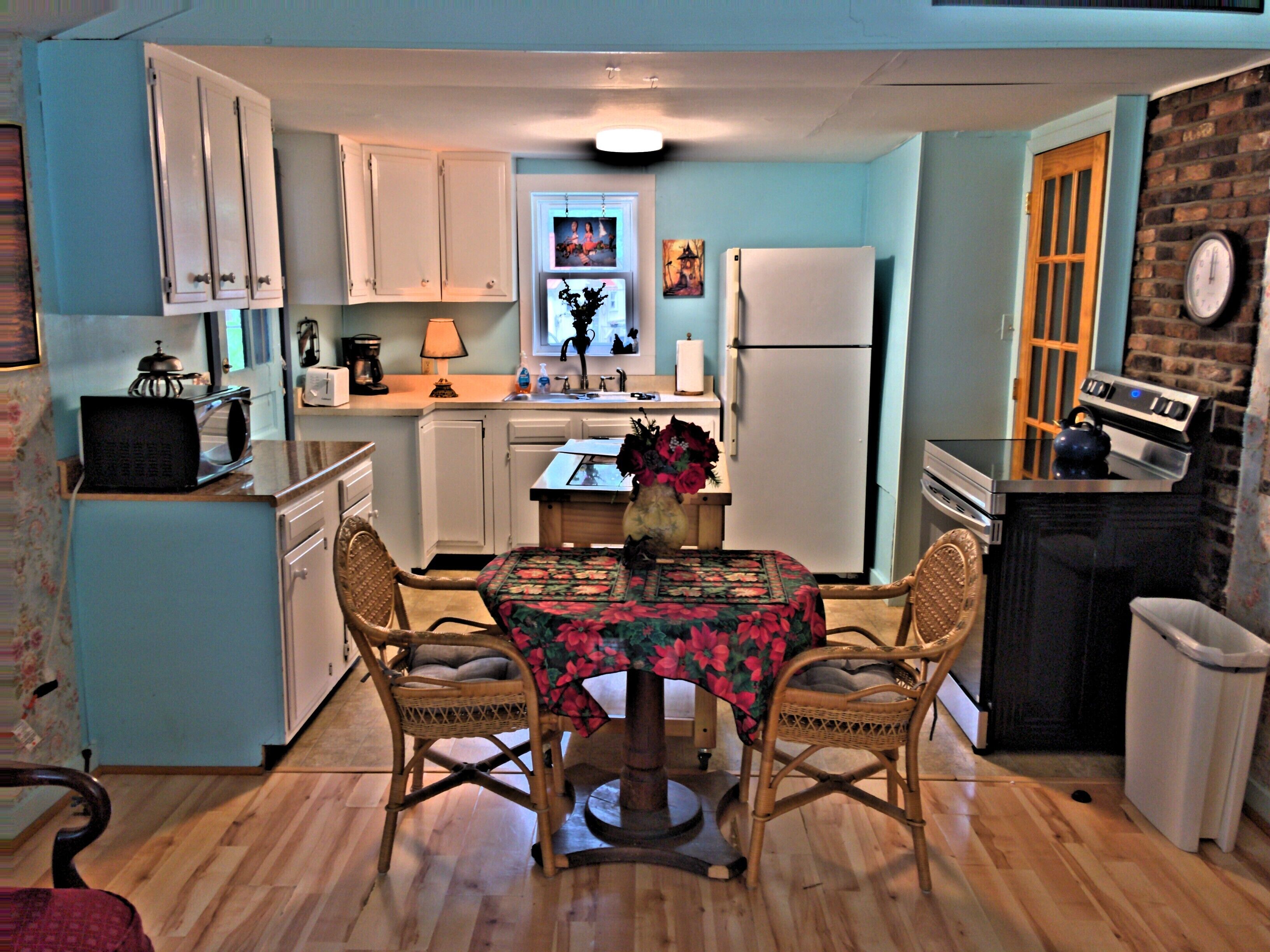 A compact kitchen with white cabinets, a refrigerator, a stove, and a dining table with chairs.