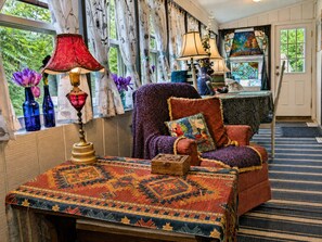 A cozy room with a patterned rug, a chair with a cushion, a table with a lamp, and a window with curtains. - Dawson’s Diggs:  Causeway, Lake Access & Kayaks (Colchester)