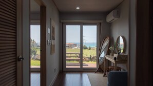 Une pièce dotée d’un plancher en bois, d’un bureau avec un miroir et offrant une vue sur un jardin et un plan d’eau, grâce à une porte coulissante.