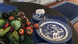 A kitchen with white cabinets, a red kettle, and a dining area with a blue tablecloth and traditional blue and white plates.
