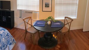 A dining area with a round table, two chairs, a small potted plant, and a framed picture on the wall.