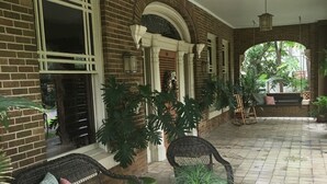 A covered patio area with wicker furniture, potted plants, and a tiled floor.