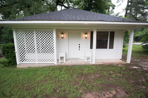 A small, single-story house with a white exterior, a dark roof, and a front porch with two steps.