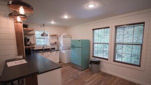A kitchen with white cabinets, a black countertop, a teal refrigerator, and a window with blinds. - Detached Cottage In A Rural Woodsy Neighborhood. (Shreveport)