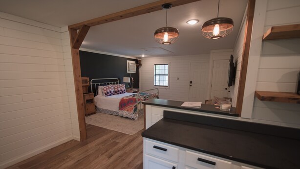 A bedroom with a bed, bedside table, and a nightstand. There is a window and a door in the room. - Detached Cottage In A Rural Woodsy Neighborhood. (Shreveport)