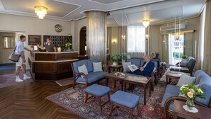 A hotel lobby with a reception desk, seating area with sofas and armchairs, a bar, and a large mirror. - Hotel Brack (Munich)