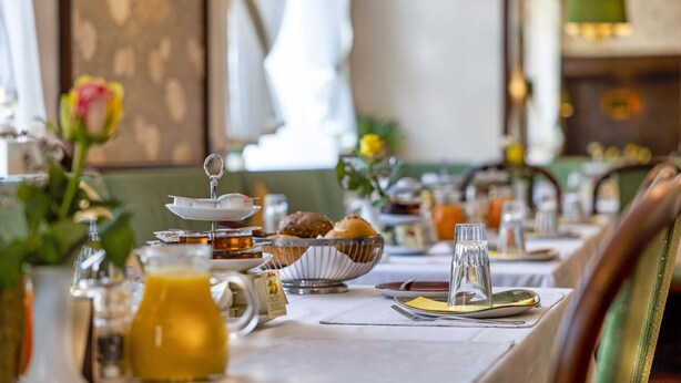 A breakfast setting with a table set for two, including a bowl of bread, a jug of orange juice, and a teapot. - Hotel Brack (Munich)