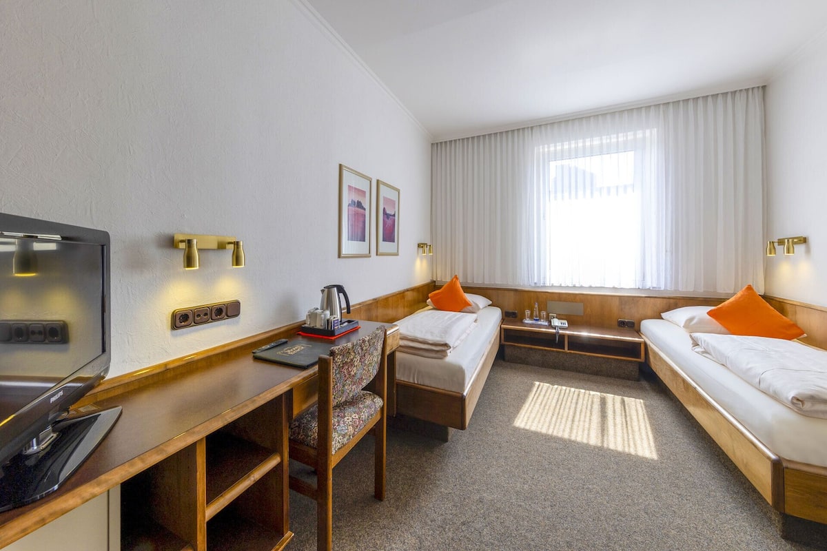 Habitación de hotel con dos camas, un escritorio con televisor y una ventana con cortinas.