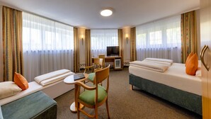 A hotel room with a bed, a sofa, a desk with a chair, a television, and a small table. - Hotel Brack (Munich)