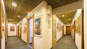 A hotel corridor with framed artwork on the walls, carpeted floors, and wooden doors. - Hotel Brack (Munich)
