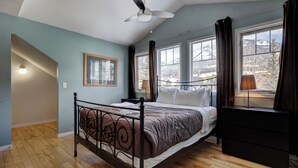 A bedroom with a bed, a ceiling fan, a dresser, and large windows with curtains. - Summit Place 2B | Excellent Location, Amazing Views (Canmore)