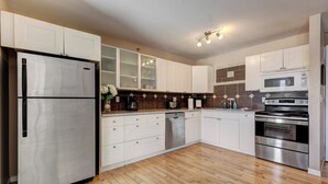 A modern kitchen with white cabinets, stainless steel appliances, and a wooden floor. - Summit Place 2B | Excellent Location, Amazing Views (Canmore)