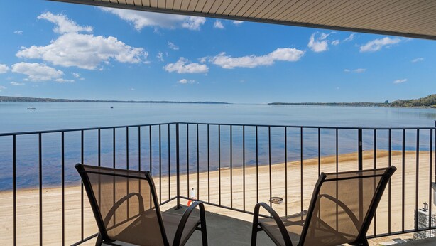 En balkon med to stole, udsigt over et roligt vand og en sandstrand.