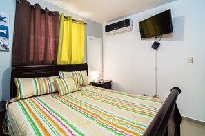 Une chambre à coucher avec un lit, des rideaux, un téléviseur et un appareil de climatisation.
