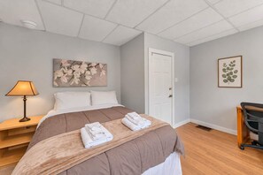 A bedroom with a bed, a nightstand, a lamp, a door, and a chair.