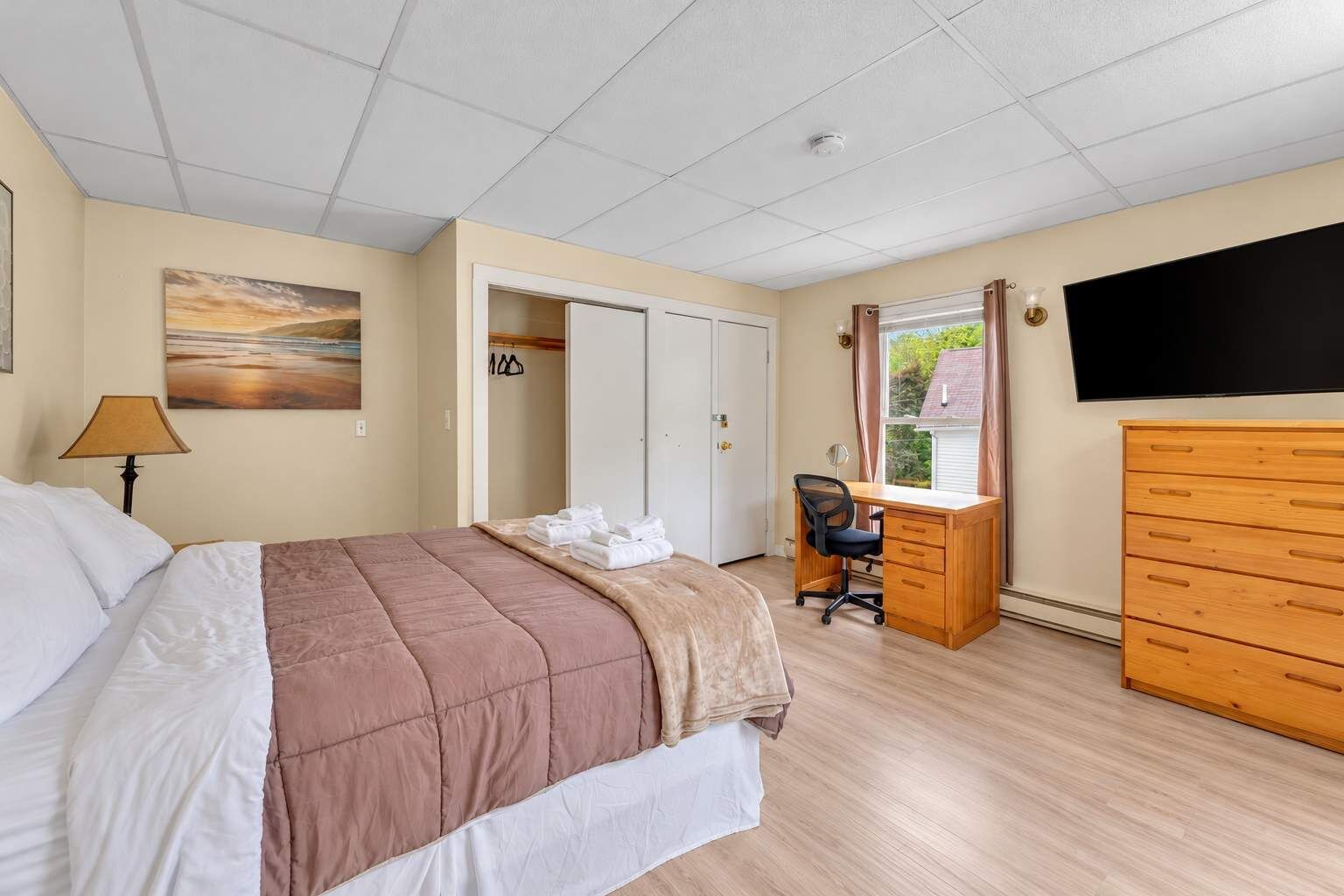 A bedroom with a bed, desk, dresser, and a TV.